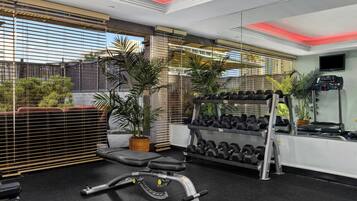 Ein modernes Fitnessstudio mit Trainingsgeräten, einem Fernseher und großen Fenstern mit Jalousien.