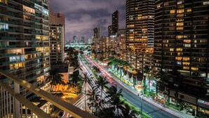 Un paisaje urbano nocturno con rascacielos, una calle concurrida con estelas de luz y un puente a lo lejos.