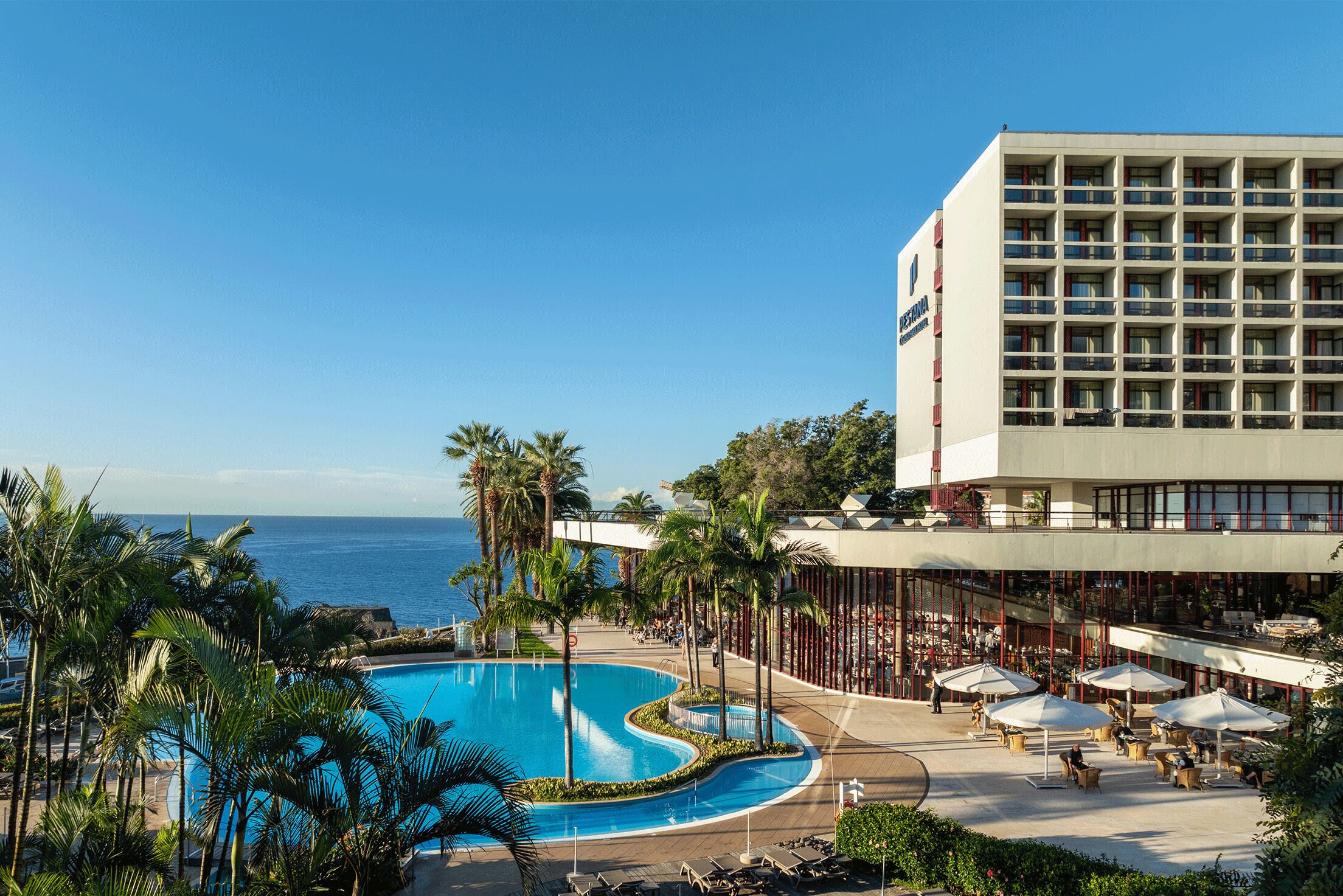 Um hotel com piscina, palmeiras e vista para o oceano.