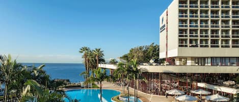 Um hotel com piscina, palmeiras e vista para o oceano.