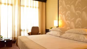A hotel room with a large bed, a chair, a bedside table, and a lamp.