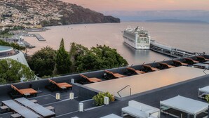 A rooftop terrace with lounge chairs and tables, overlooking a coastal cityscape and a cruise ship. - Pestana Casino Park Ocean and SPA Hotel (Funchal)