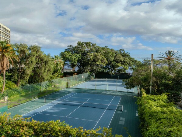Una cancha de tenis al aire libre rodeada de abundante vegetación y árboles.