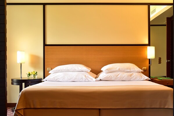 A neatly made double bed with white linens, a wooden headboard, and two bedside lamps.
