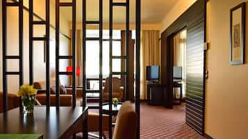 Habitación de hotel con sala de estar que incluye un sofá, una mesa de centro con un florero y un mueble para televisión, además de una alfombra estampada.