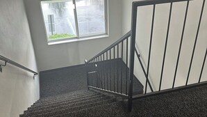 A staircase with a handrail, carpeted steps, and a window with a view of the outside. - Motel 6 Anderson, IN - Indianapolis (Anderson)