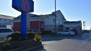 A motel sign with the number 6, a parking lot, and a building with a red and white facade. - Motel 6 Anderson, IN - Indianapolis (Anderson)