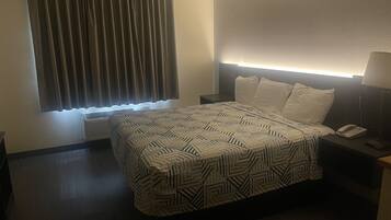 A hotel room with a bed, bedside table, lamp, and a window with curtains.