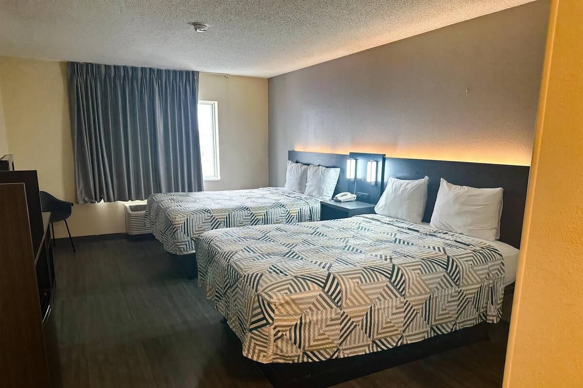 A hotel room with two beds, a desk, and a chair.
