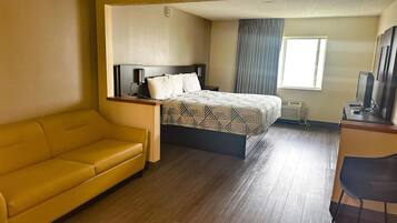 A hotel room with a bed, a yellow sofa, a desk with a computer, and a window with curtains.
