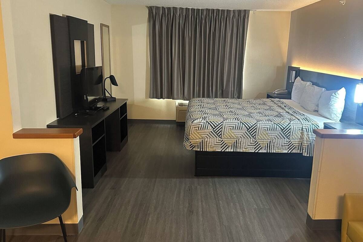 A hotel room with a bed, a desk with a computer, a chair, and a TV.