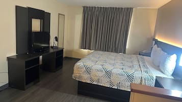 A hotel room with a bed, a TV on a stand, a desk, and a large window with curtains.