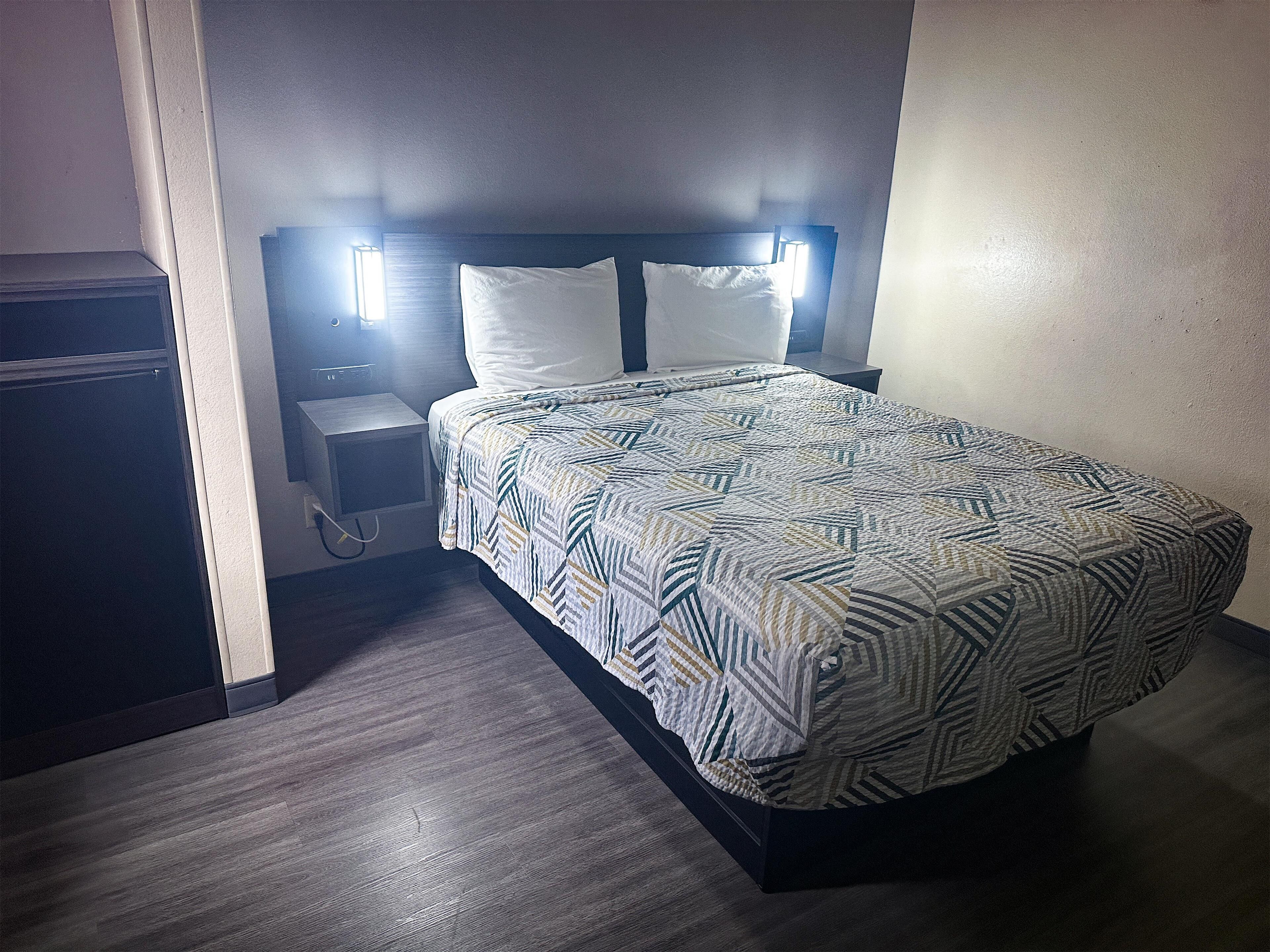A hotel room with a bed, a nightstand, and a lamp.