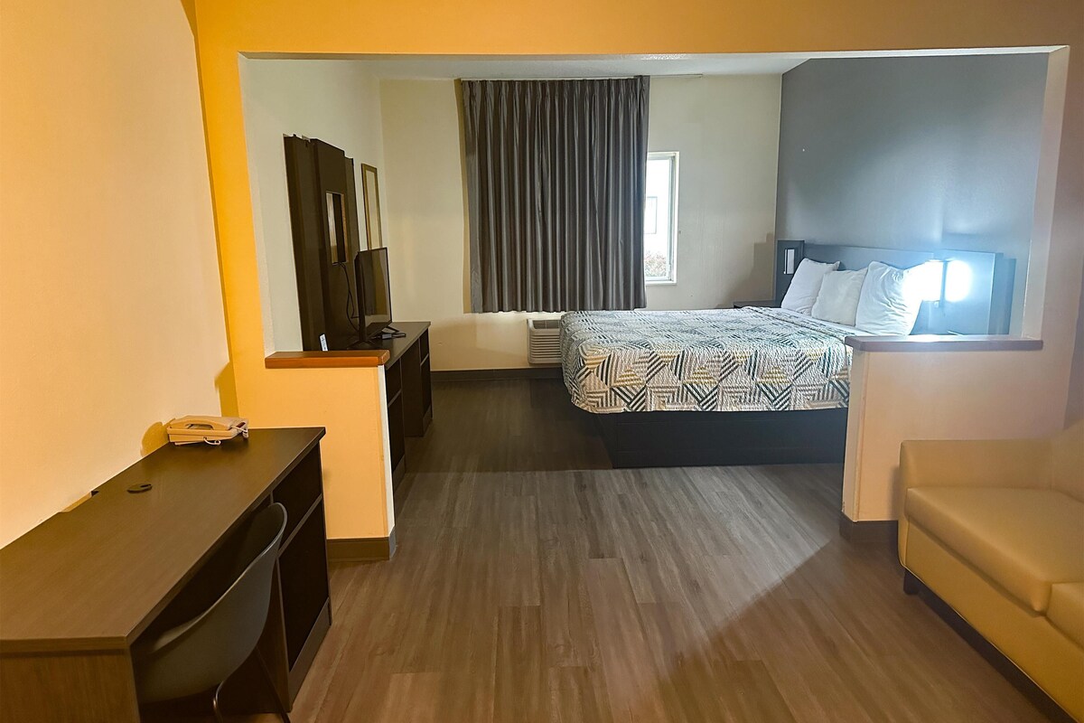 Habitación de hotel con cama, escritorio, silla, televisor y ventana con cortinas.
