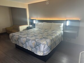 Une chambre d’hôtel avec un grand lit, une table de chevet avec une lampe, une chaise et un téléphone fixé au mur.
