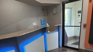 A reception area with a counter, blue lighting, a fire alarm, and a clock on the wall. - Motel 6 Anderson, IN - Indianapolis (Anderson)