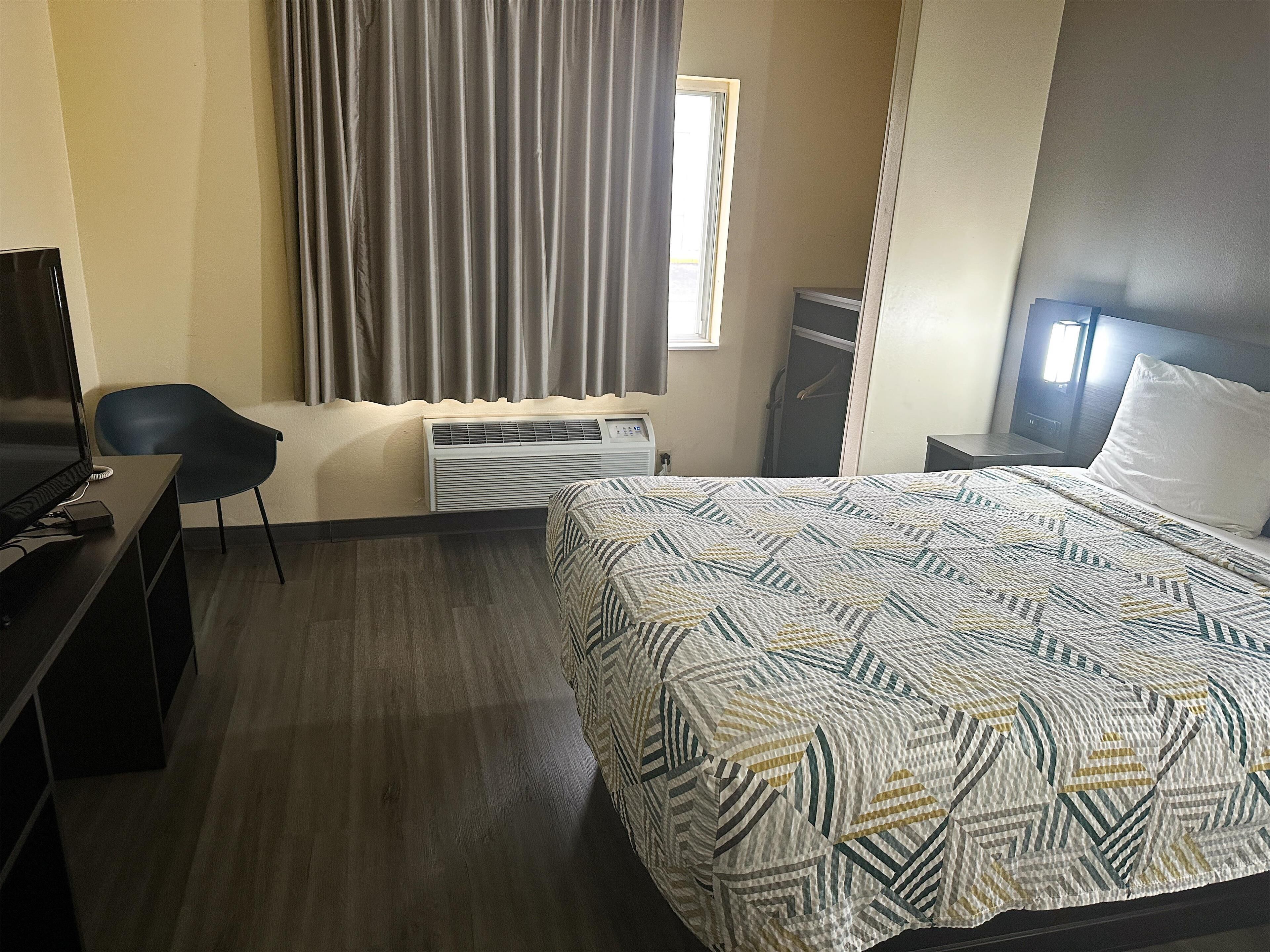 Una habitación de hotel con cama, escritorio con computadora, silla, ventana con cortinas y armario.