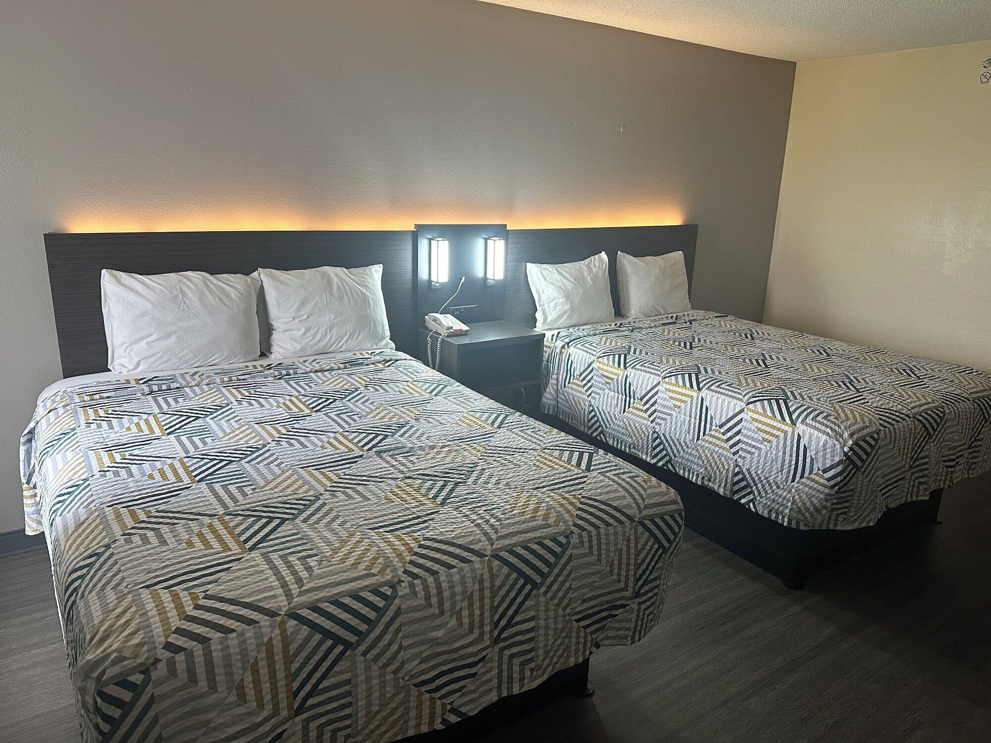 Una habitación de hotel con dos camas, cada una con ropa de cama estampada, una mesita de noche con lámpara y un teléfono en la pared.
