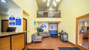 A hotel reception area with a check-in counter, a sofa, a small table with a plant, and a sign for Days Inn. - Days Inn by Wyndham Evansdale Waterloo (Evansdale)