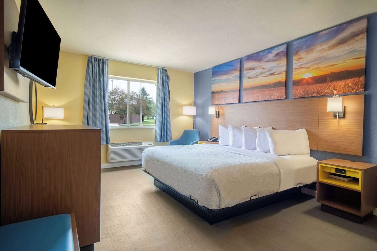 A hotel room with a bed, bedside tables, a TV, and artwork on the wall.