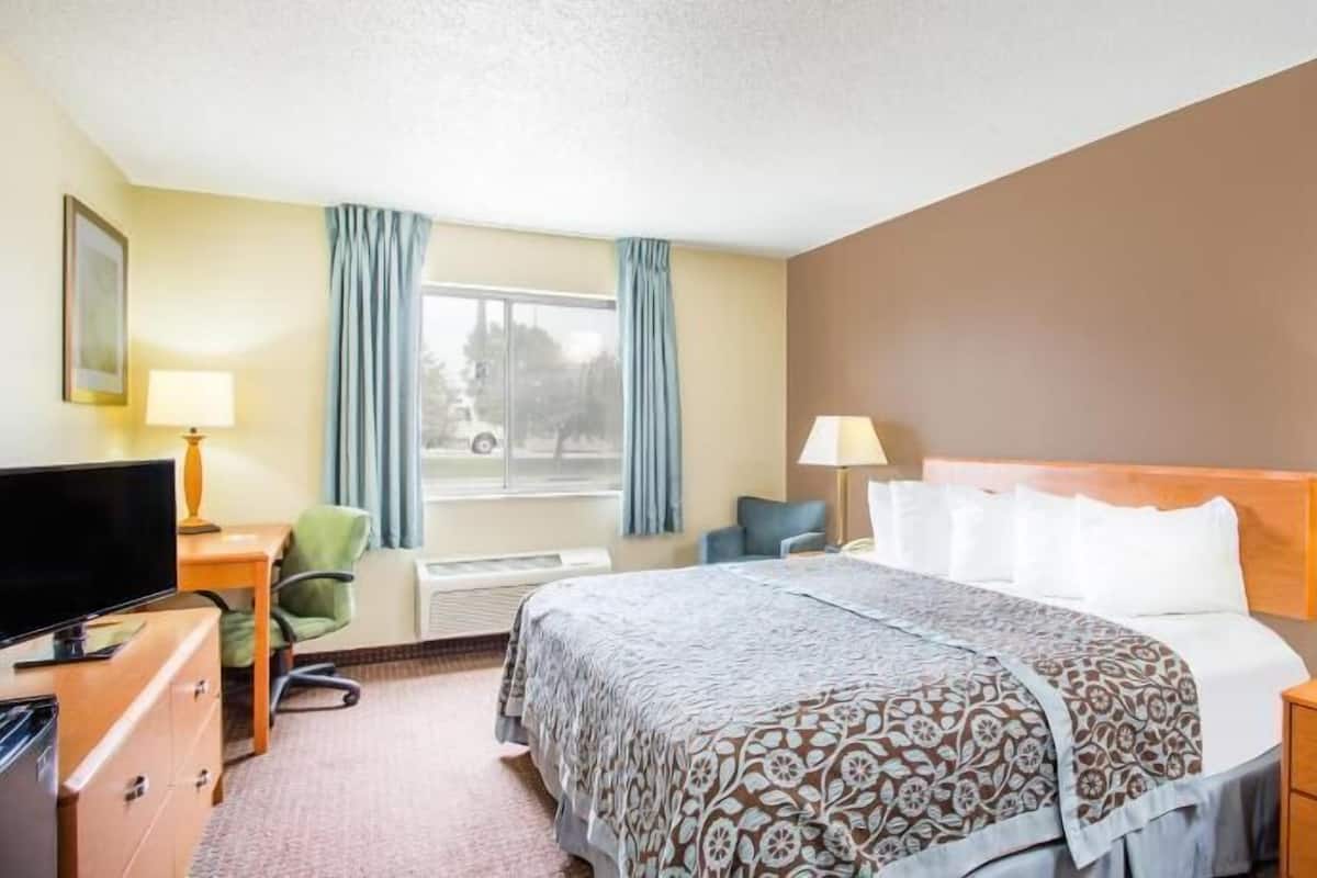 A hotel room with a bed, two bedside lamps, a desk with a television, a chair, and a window with curtains.