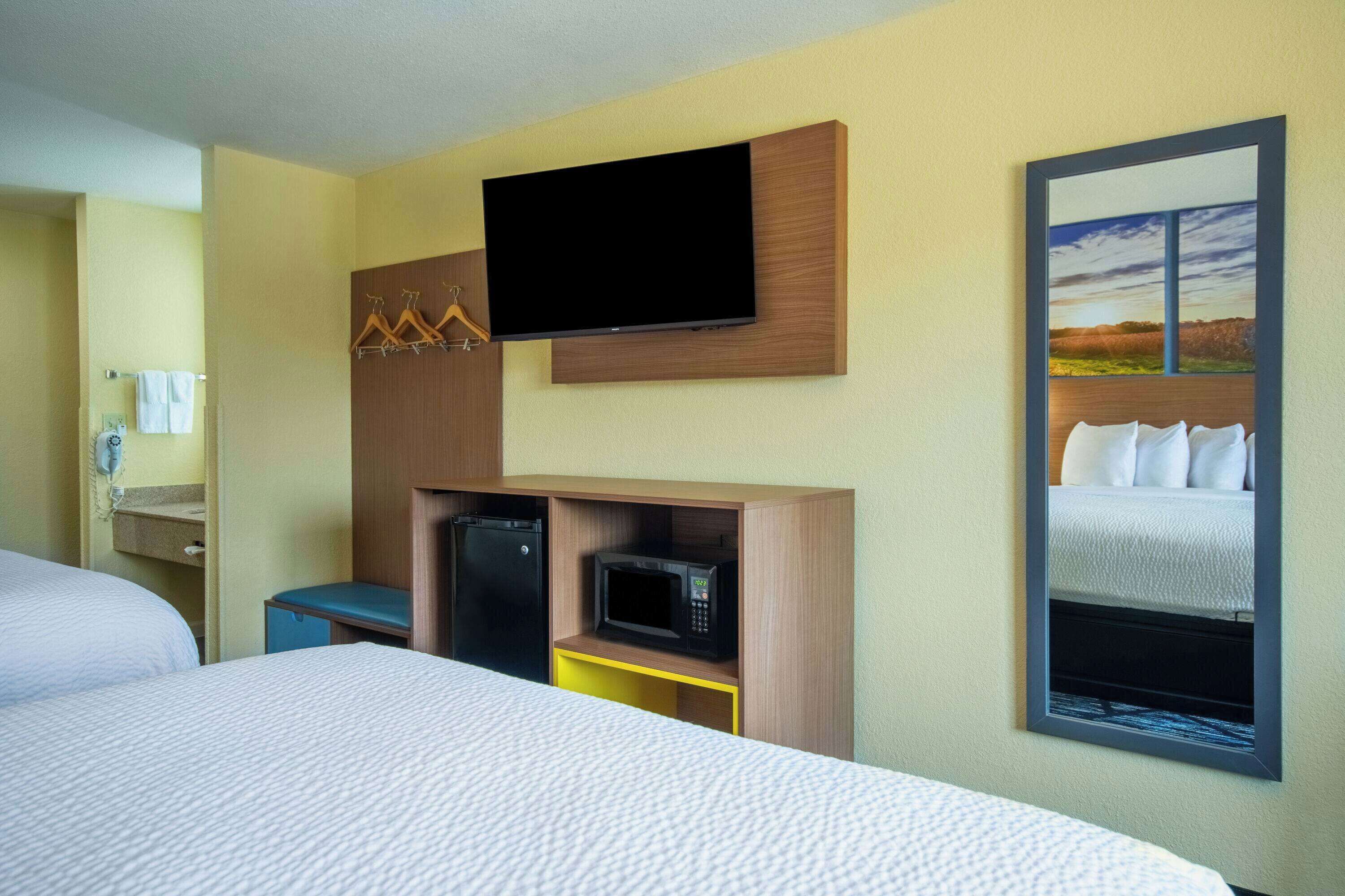 A hotel room with a bed, a TV mounted on the wall, a microwave, and a small cabinet.