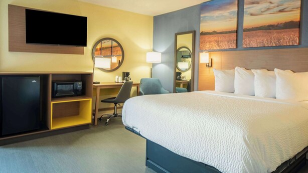 A hotel room with a large bed, a desk with a computer, a TV, and a microwave. - Days Inn by Wyndham Evansdale Waterloo (Evansdale)