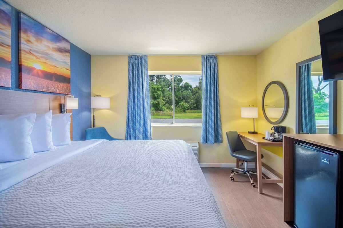 A hotel room with a large bed, a desk, a chair, a television, and a window with curtains.