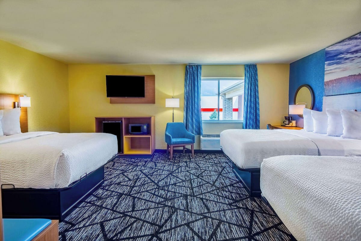A hotel room with two beds, a desk, a chair, a flat-screen TV, and a window with curtains.