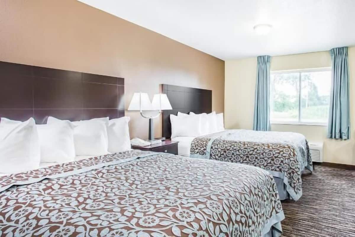 A hotel room with two beds, a desk with a lamp, a chair, and a TV.
