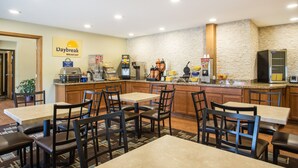 A breakfast area with a stone wall, wooden tables and chairs, a coffee station, and a sign for Daybreak Breakfast. - Days Inn by Wyndham Evansdale Waterloo (Evansdale)