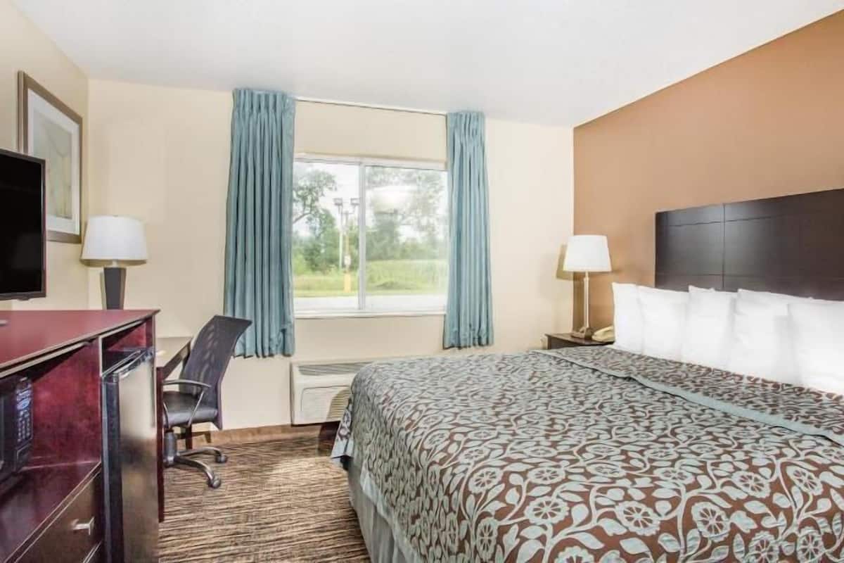 A hotel room with a bed, desk, chair, TV, and a window with curtains.