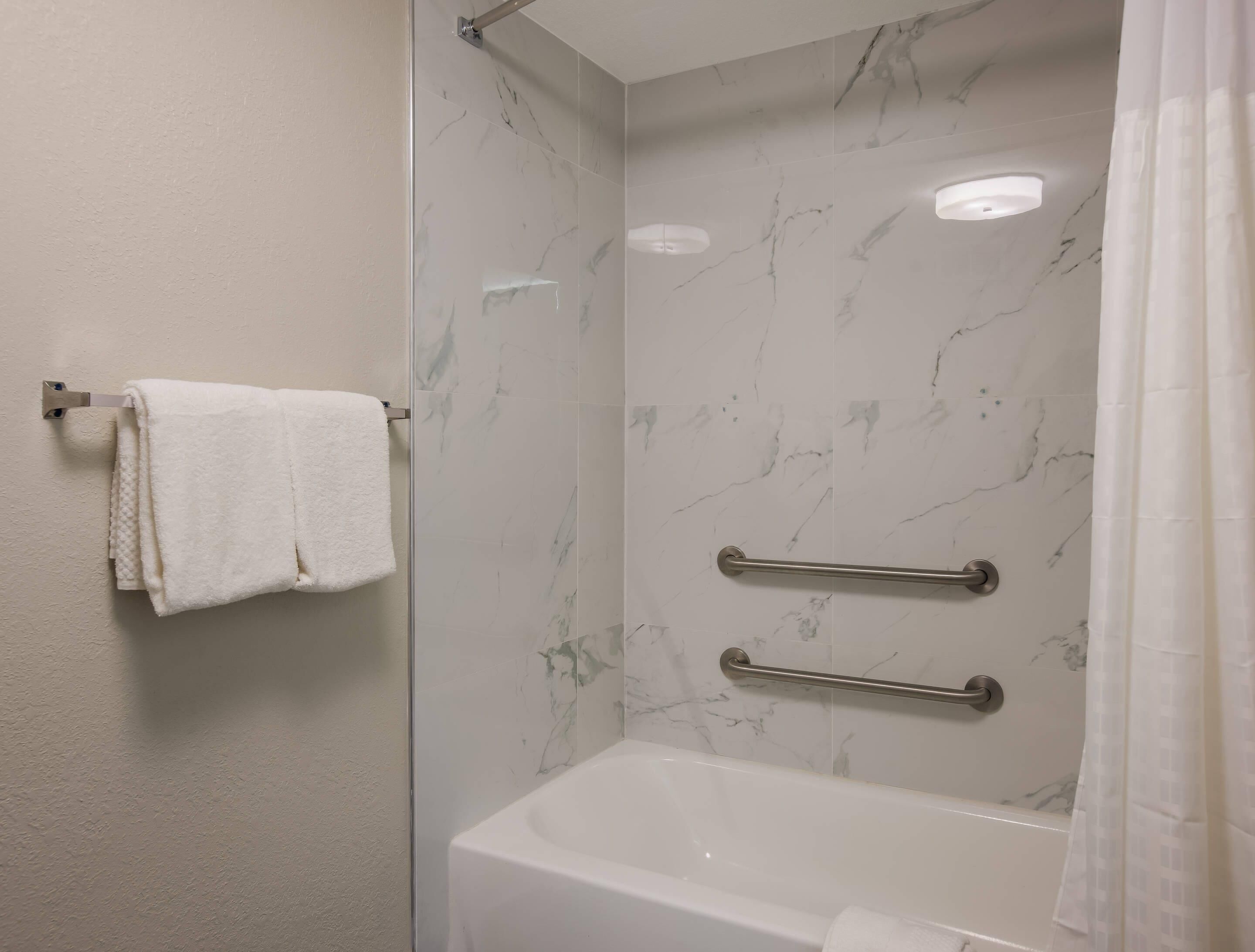 A bathroom with a white bathtub, marble walls, a towel rack, and a grab bar.