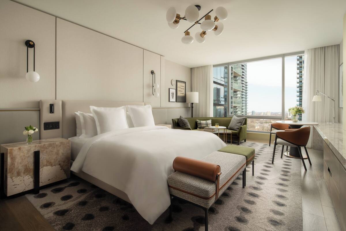 A modern hotel room with a large bed, a desk, a sofa, and a view of the city.