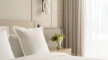 Una cama bien hecha con sábanas blancas, una mesita de noche con un florero y una lámpara de pared.