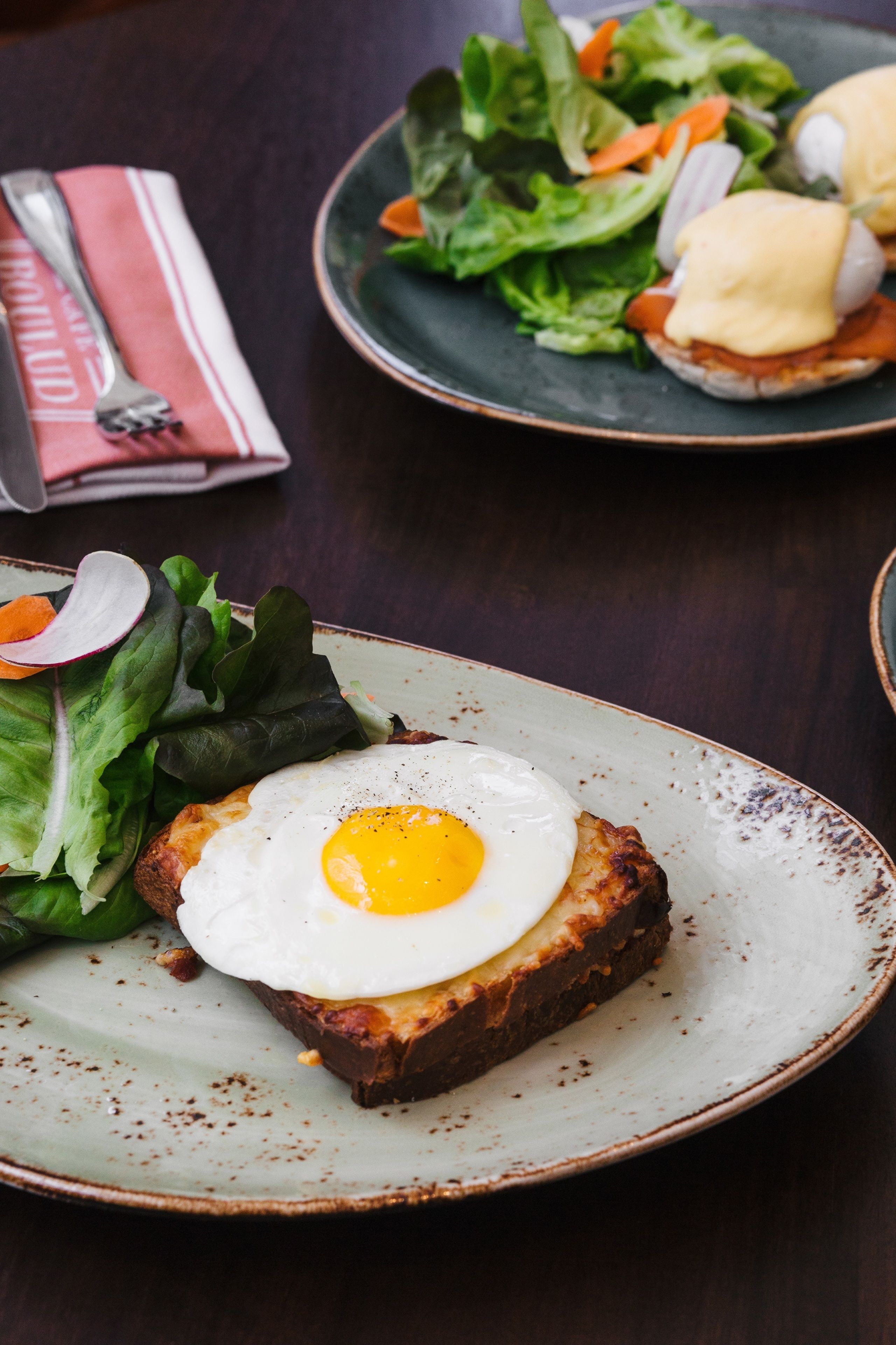 A plate with a fried egg on toast, a side salad, and a folded napkin with a fork.