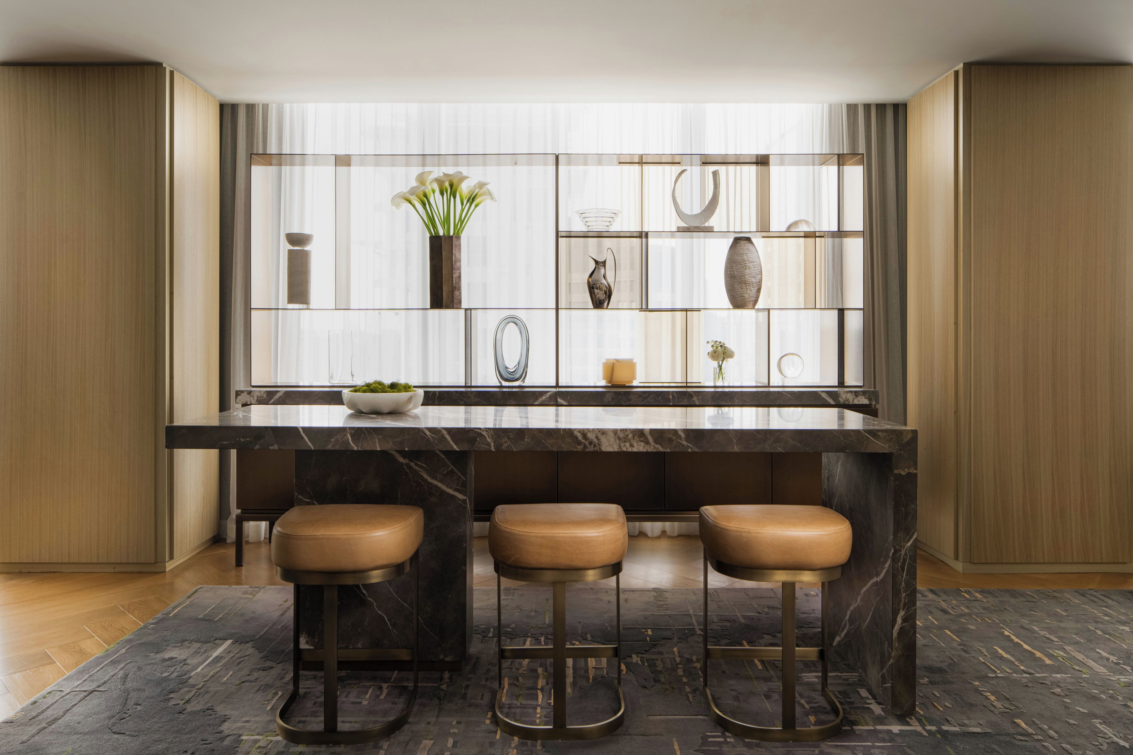 Een moderne keuken met een marmeren aanrecht, drie krukken en een decoratieve plank met diverse spullen.