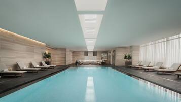 Une piscine intérieure moderne, dotée de chaises longues et d’un canapé, et entourée de murs en bois et de grandes fenêtres.