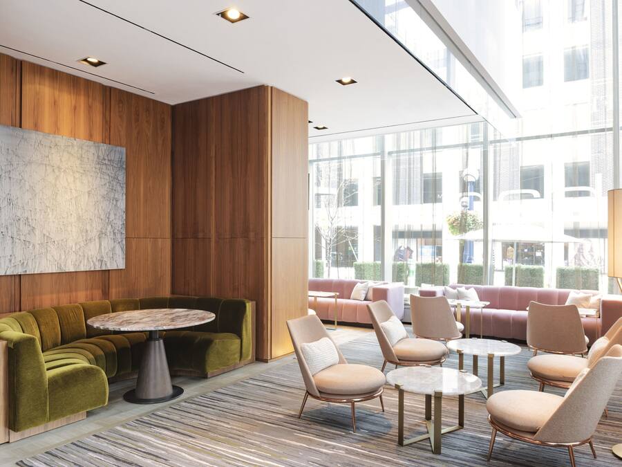 Un espacio lounge moderno con una mesa redonda, sofás y sillones, paneles de madera y ventanas amplias con vistas a la ciudad.