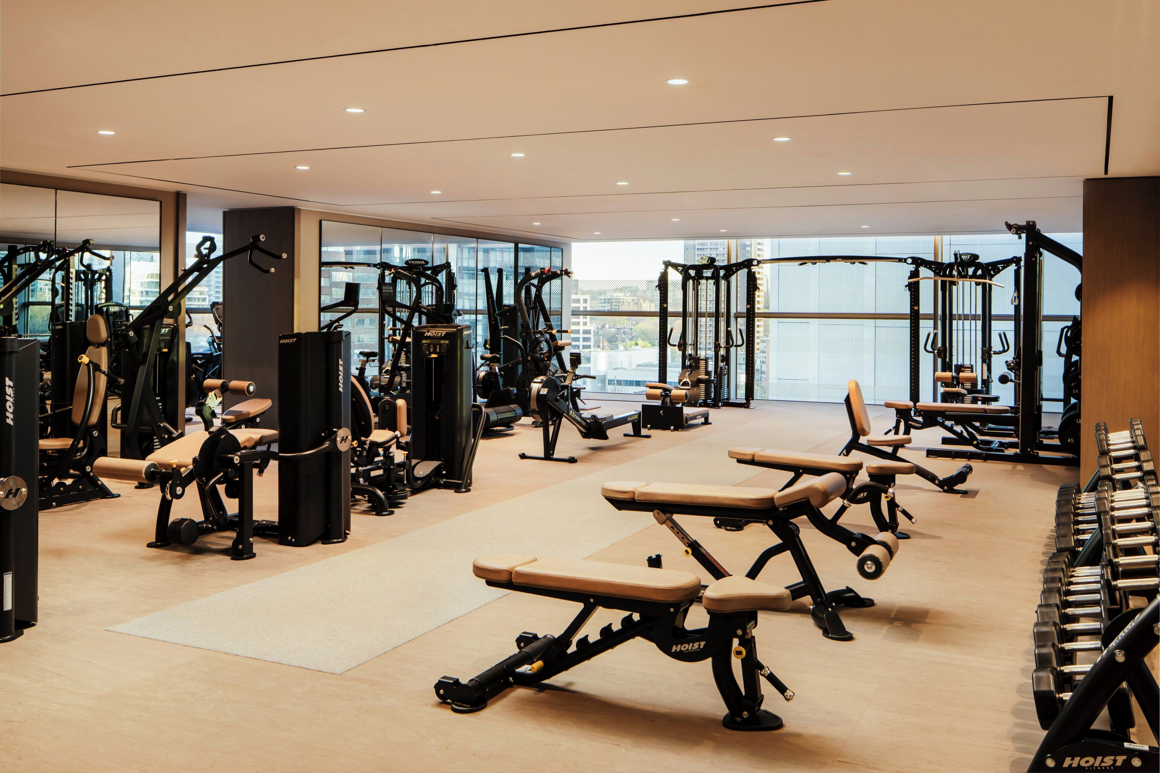Ett modernt gym med olika typer av träningsutrustning, stora fönster och en ren och rymlig inredning.
