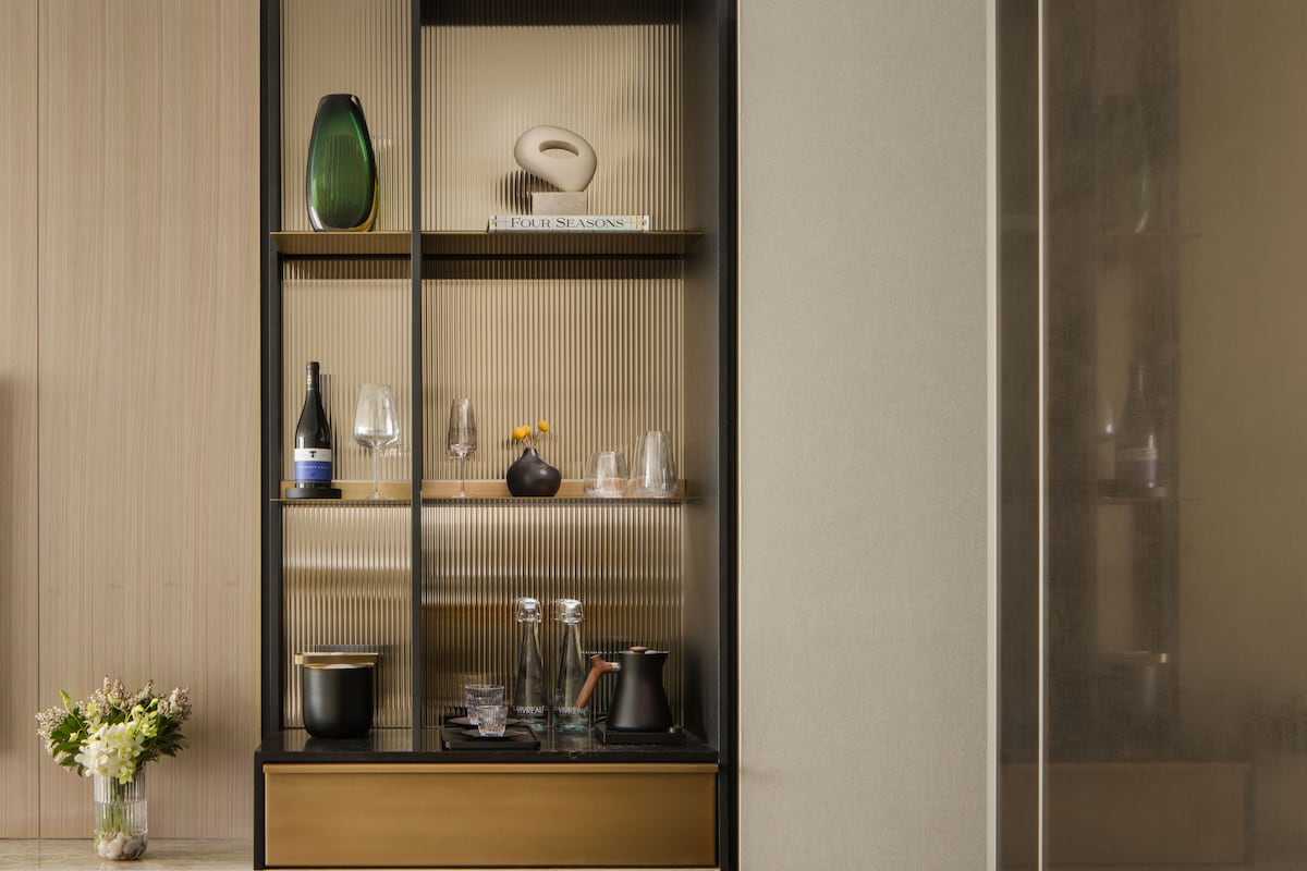 Un intérieur moderne avec un mur recouvert de panneaux en bois, une étagère décorative à cadre noir où sont exposés divers objets, et un petit vase avec des fleurs placé à gauche.