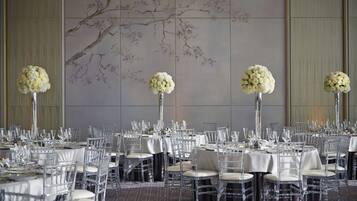 A banquet hall with round tables set for dining, clear chairs, and floral centerpieces.
