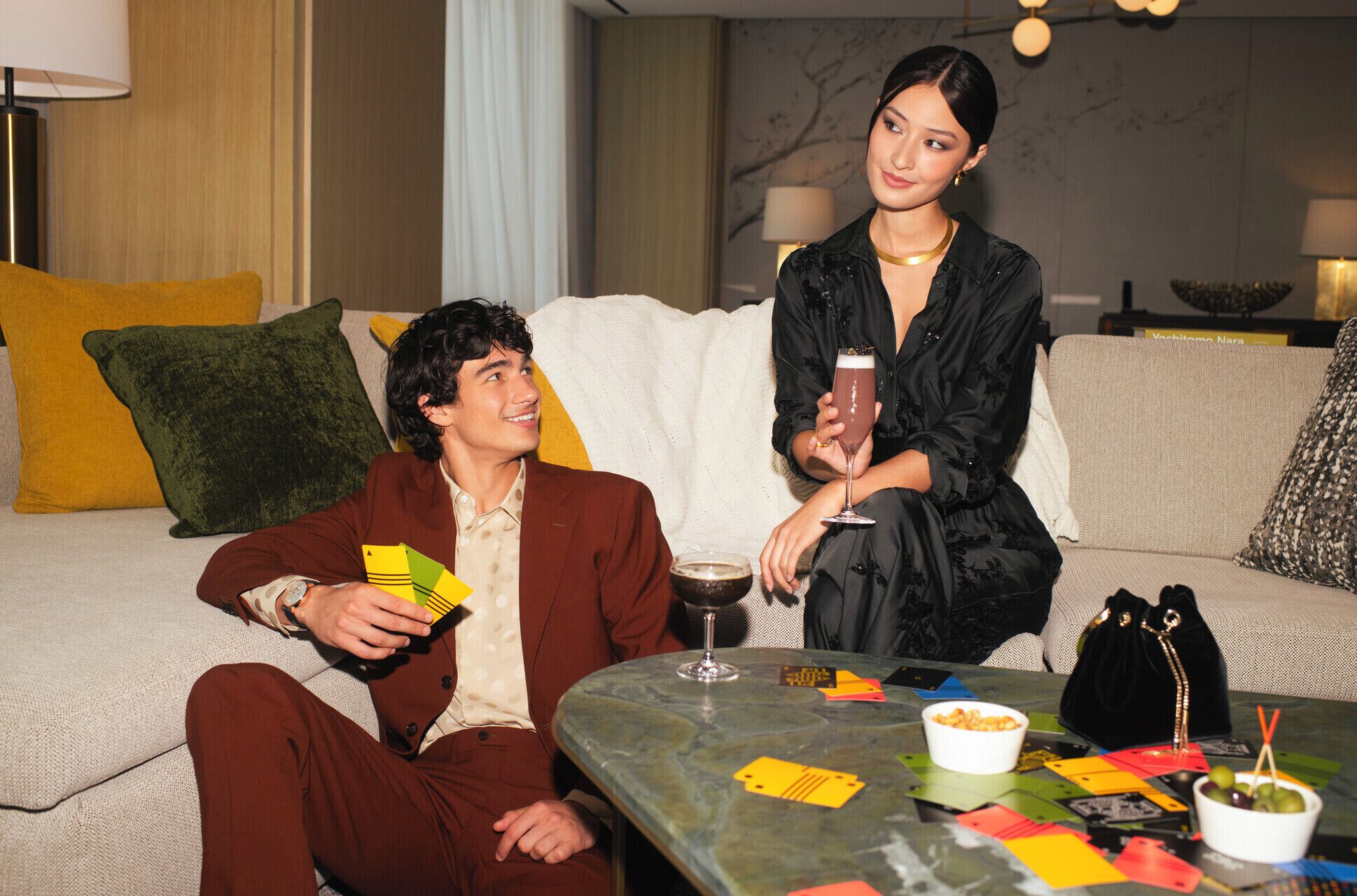 A modern living room with a sofa, a coffee table with cards and a glass, and a lamp.