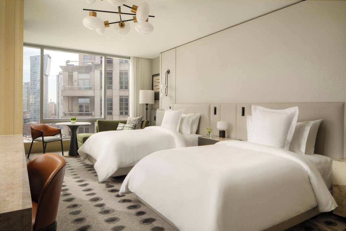 A hotel room with two beds, a dining table, and a view of the cityscape.