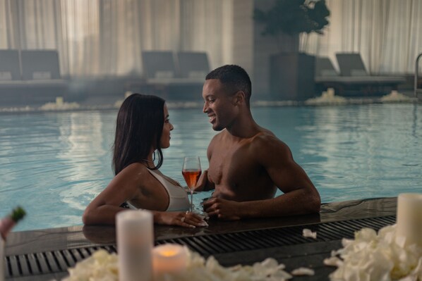 Un couple dans une piscine, avec une table, des bougies et un verre à cocktail.