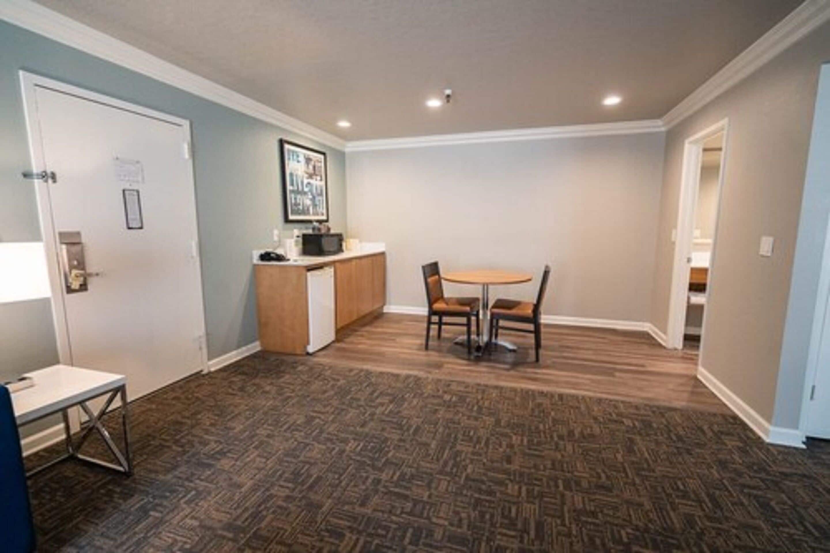 A room with a herringbone-patterned floor, a small table with chairs, a microwave, and a framed picture on the wall.