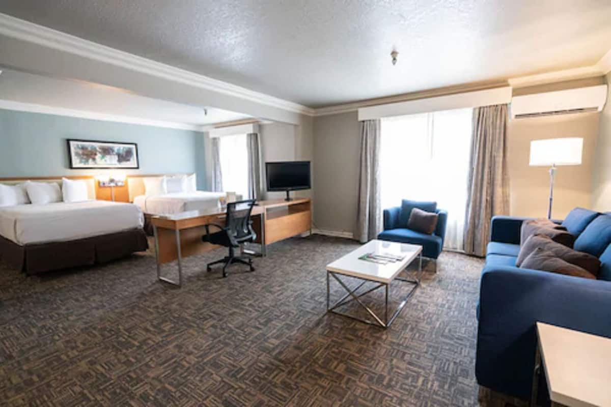 A hotel room with a bed, desk, TV, and seating area.