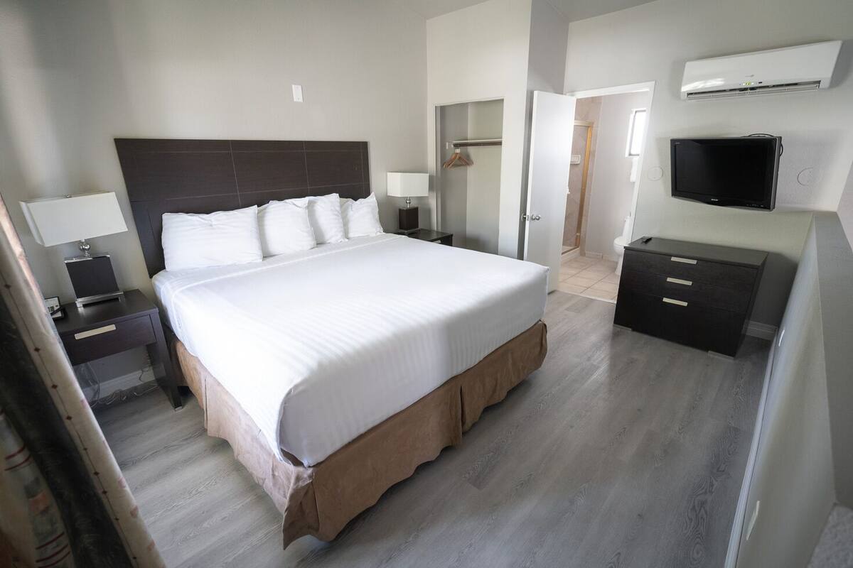 A hotel room with a large bed, bedside tables, a TV, and a wardrobe.