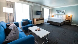 A hotel room with a bed, a desk, a chair, a TV, and a window with curtains. - Alexis Park All Suite Resort (Las Vegas)