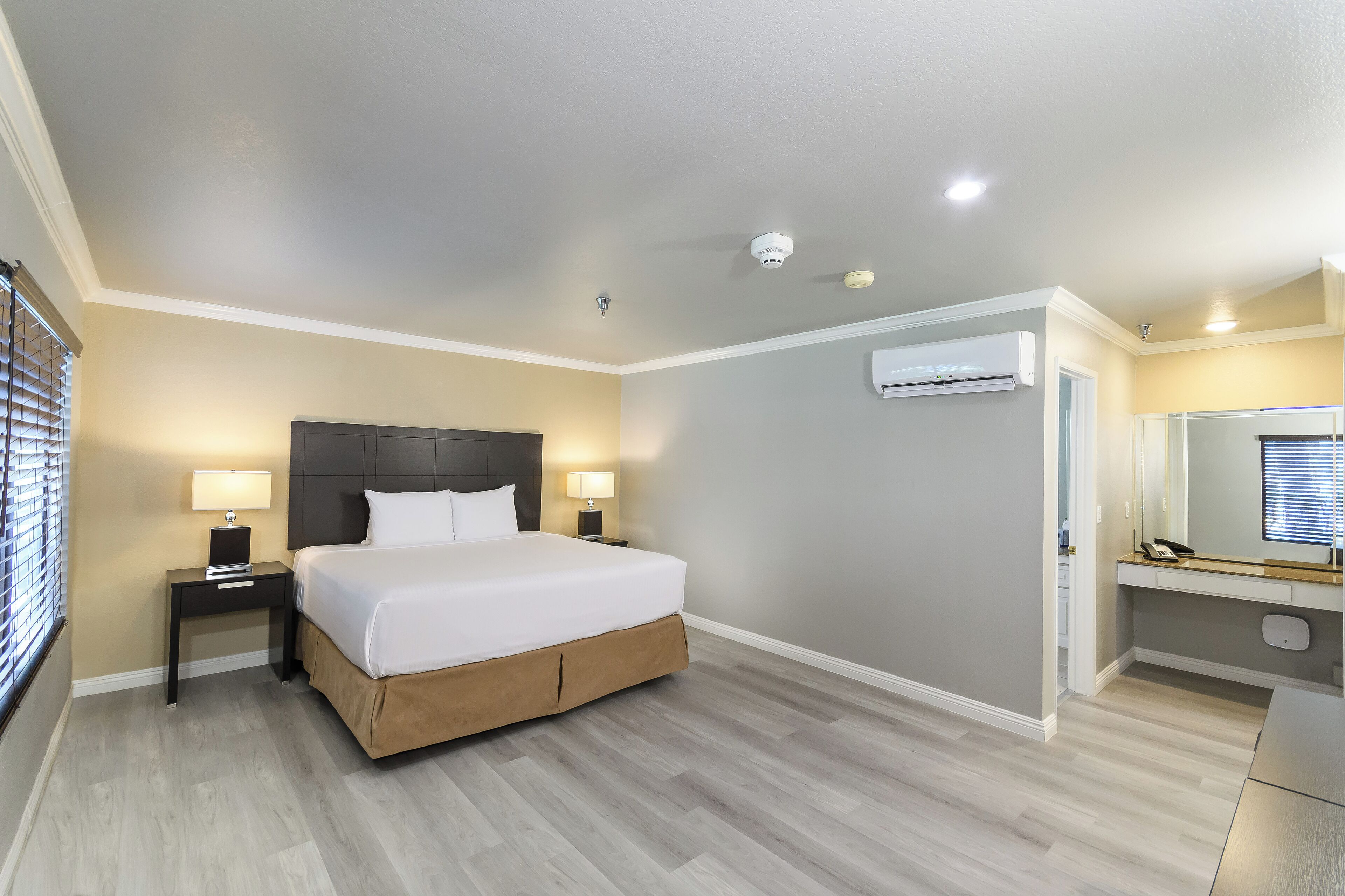 A modern hotel room with a large bed, bedside lamps, an air conditioning unit, and a small desk with a mirror.